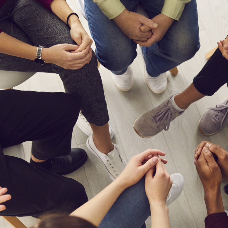 Top view of diverse people sitting in a close circle and talking to a therapist. Cropped image of unidentified people receive help and support during a group therapy session. Concept of group therapy.
